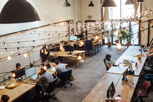 Collaborative tech workspace with wooden desks, string lights, and professionals working on secure enterprise systems